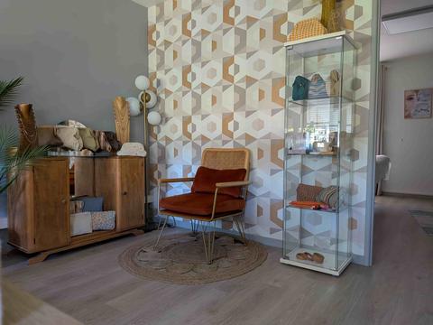 Accueil de l'institut : fauteuil en velours terracotta sur un tapis rond en jute, papier peint à hexagones or et beige, buffet en bois et vitrine de pochettes