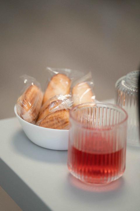 Verre strié d'infusion rouge posé sur une tablette, à côté d'un bol blanc de madeleines emballées