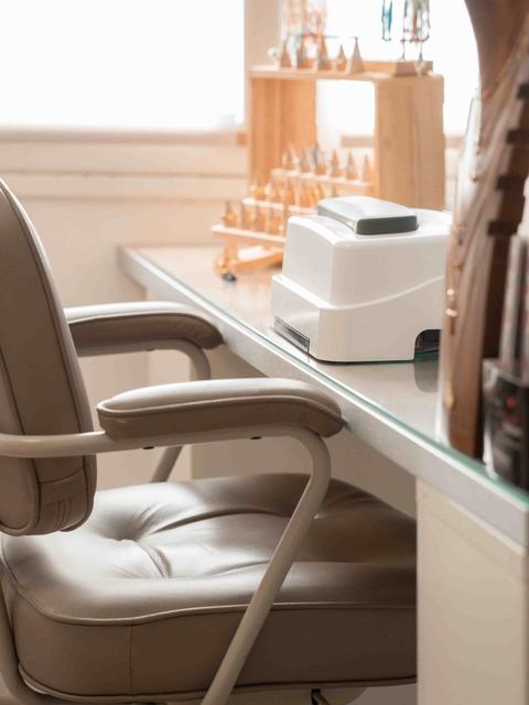 Poste d'onglerie : fauteuil en cuir beige devant une tablette en verre, lampe à ongles blanche et présentoirs en bois clair