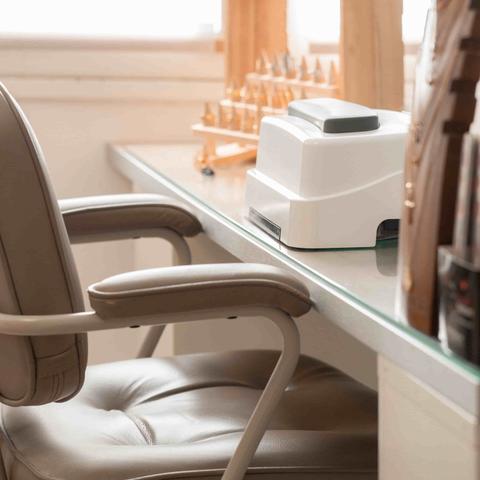 Poste d'onglerie : fauteuil en cuir beige devant une tablette en verre, lampe à ongles blanche et présentoirs en bois clair