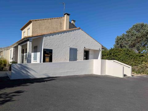 Façade blanche de l'institut sous un ciel bleu : maison méditerranéenne aux volets gris-bleu, muret blanc et parking au premier plan