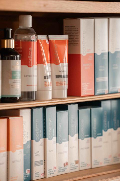 Étagère en bois garnie de soins Corême : flacon de lotion, tubes de gel orange et boîtes blanches, corail et bleu canard