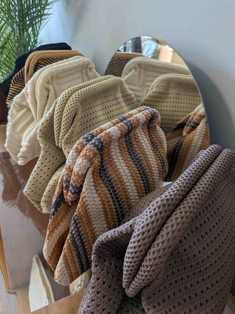 Pochettes en maille tricotée, écrue, beige, rayée et taupe, alignées devant un miroir ovale