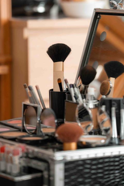 Mallette de maquillage ouverte : pinceaux dans des pots noirs, miroirs de poche, fards et rouges à lèvres