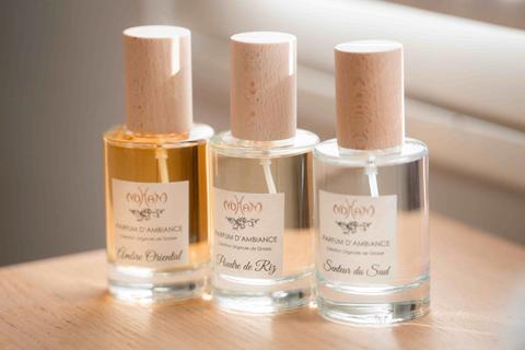 Trois flacons de parfum d'ambiance à bouchon de bois clair posés sur une table : Ambre oriental, Poudre de riz et Senteur du Sud