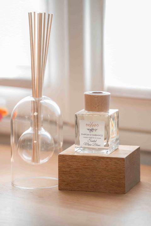 Diffuseur de parfum d'ambiance Santal Musc blanc posé sur un cube de bois, bâtonnets en rotin dans une carafe en verre à côté